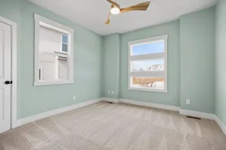 Plush carpet flooring, contemporary ceiling fan with integrated lighting, multiple windows providing natural light, and a crisp white trim package