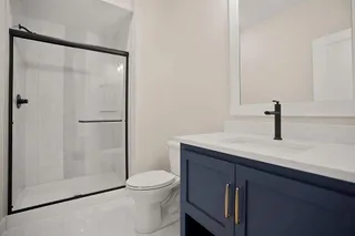 Bathroom featuring a shower with a sliding glass door, a modern vanity with a white countertop and integrated sink, a dark blue cabinet with gold-toned hardware, and a framed mirror