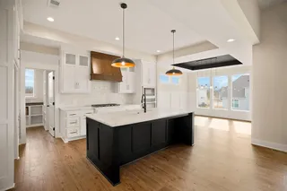 Spacious kitchen featuring an expansive center island, white cabinetry, wood-finish flooring, and a white tile backsplash