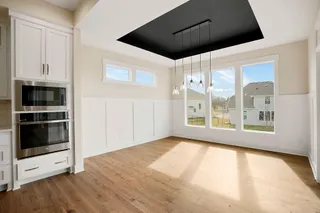 Built-in stainless steel double oven, white shaker cabinetry with brushed nickel hardware, expansive windows, recessed ceiling with pendant lighting, and wood-finish flooring