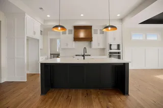 Open-concept kitchen with a large center island, white cabinetry, integrated appliances, wood-finish flooring, and a decorative wood range hood