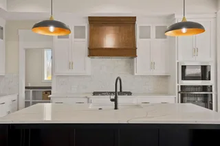 Kitchen island with a light-toned countertop, white cabinetry with gold-toned hardware, a wood-finish range hood, and integrated stainless steel appliances