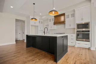 Kitchen featuring a dark-toned island with a light-toned countertop, wood-finish flooring, white cabinetry, and stainless steel appliances