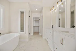 Freestanding soaking tub, dual vanity with quartz countertops, large framed mirrors, walk-in shower, and built-in closet shelving