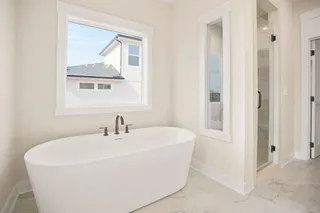Freestanding soaking tub with a dark-finish fixture, glass-enclosed shower with a dark-finish frame, and light-toned tile flooring