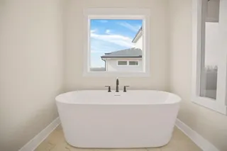 Freestanding soaking tub with matte black fixtures, set against light-toned walls and tile flooring
