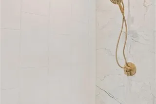 Shower featuring large format white wall tiles, a built-in bench with veined tile, and a gold-tone shower head