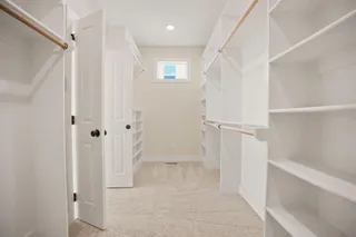 Spacious walk-in closet featuring built-in shelving, hanging rods, recessed lighting, and a window for natural illumination