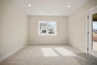 Recessed lighting, neutral wall tones, carpeted flooring, a window with white trim, and a glass-paneled door leading to an exterior concrete patio