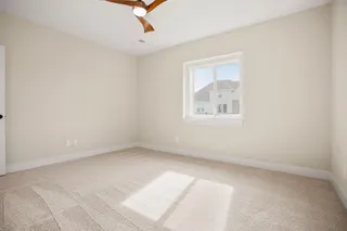 Spacious room featuring neutral carpet, a contemporary ceiling fan with wood-finish blades, and a large window with white trim