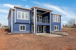 Blue horizontal siding, white trim, multiple large windows, covered balcony with black railing, concrete patio