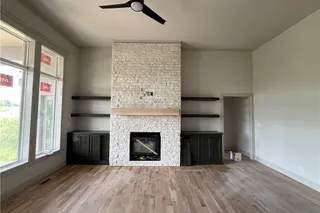 Stone-clad fireplace with a wood mantle, built-in cabinetry, and floating shelves. Home Under  Construction. OCTOBER 2026 COMPLETION, PHOTO IS OF ACTUAL HOME.