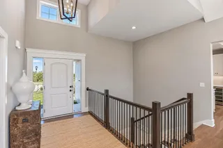 A soaring entry showcases a vaulted ceiling, wood flooring, and a modern stair railing. PHOTO IS OF ACTUAL HOME.