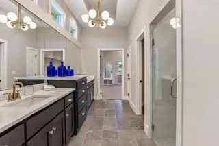 Stone counters and custom cabinetry elevate this modern bathroom featuring a tiled walk-in shower. PHOTO IS OF ACTUAL  HOME.