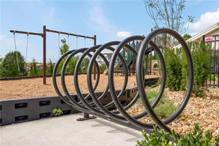 A well-equipped community play area features swings and a modern bike rack on concrete pavement.
