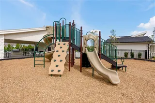 A modern community playground features a climbing wall and slide under a clear blue sky.