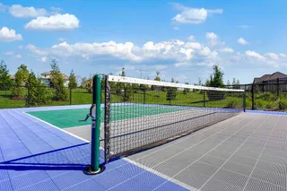 An outdoor sport court (PICKLEBALL, BASKETBALL) with professional netting stands enclosed by security fencing under blue skies.