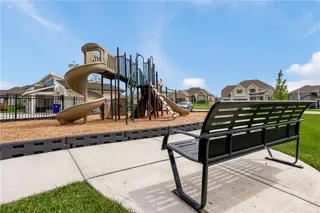 An inviting neighborhood play structure stands adjacent to a paved walkway and seating area.