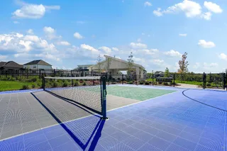 Fenced sports courts sit adjacent to a community pavilion under a clear sky.