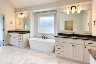An elegant soaking tub centers this dual-vanity bathroom featuring marble-patterned tile flooring. PHOTO IS OF ACTUAL HOME.