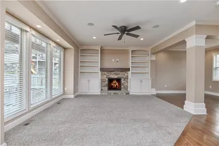 Living room with stone fireplace, custom built-ins, ceiling fan, and windows into the back yard.