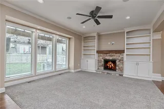 Living room with stone fireplace, built-ins, ceiling fan, and windows into the back yard.