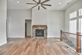 Pictures are of a Previous Model AND MAY FEATURE UPGRADES. SEVERAL BUYER SELECTIONS ARE STILL AVAILABLE. PLEASE CONTACT LISTING AGENT FOR DETAILS.Unfurnished living room featuring ceiling fan, a high ceiling, light hardwood / wood-style floors, and a stone fireplace
