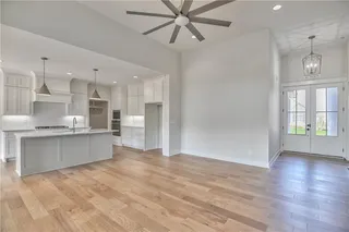 Pictures are of a Previous Model AND MAY FEATURE UPGRADES. SEVERAL BUYER SELECTIONS ARE STILL AVAILABLE. PLEASE CONTACT LISTING AGENT FOR DETAILS.Kitchen featuring white cabinetry, an island with sink, light wood-type flooring, ceiling fan with notable chandelier, and hanging light fixtures