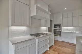 Pictures are of a Previous Model AND MAY FEATURE UPGRADES. SEVERAL BUYER SELECTIONS ARE STILL AVAILABLE. PLEASE CONTACT LISTING AGENT FOR DETAILS.Kitchen featuring appliances with stainless steel finishes, light wood-type flooring, tasteful backsplash, and white cabinetry