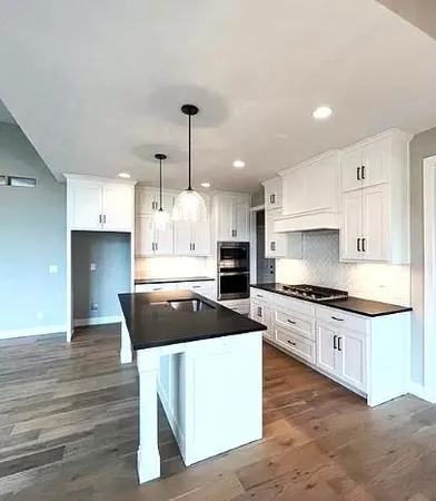 Pictures are of a Previous Model AND MAY FEATURE UPGRADES. SEVERAL BUYER SELECTIONS ARE STILL AVAILABLE. PLEASE CONTACT LISTING AGENT FOR DETAILS.Kitchen with dark hardwood / wood-style flooring, tasteful backsplash, white cabinetry, a kitchen island, and hanging light fixtures
