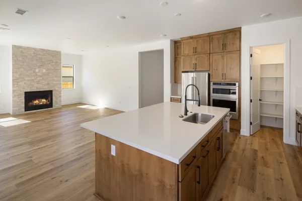 Kitchen with a white island countertop, wood cabinetry, and views into the great room with a traditional fireplace.