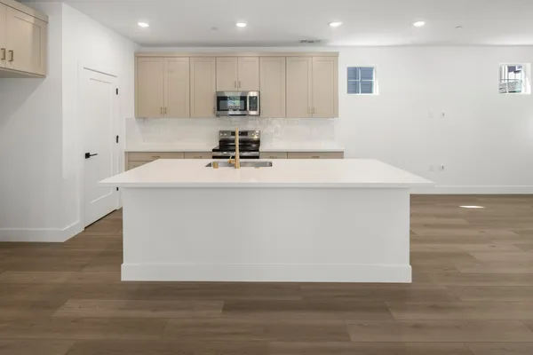 Large kitchen island with quartz countertop, light cabinetry and stainless steel appliances.