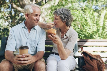 Retired couple sharing coffee and a muffin on a park bench